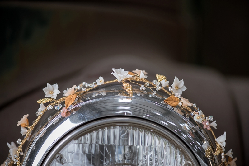 A close up of a bridal headpiece draped over the headlamp of a jeep